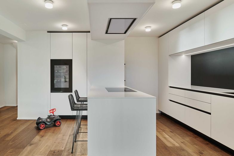 Die Küche wurde mit einem hochmodernen, minimalistischen Küchendesign von der Orea AG umgesetzt. Sie erhielt eine komplett geschlossene und grifflose Front in Matt-weiss mit schwarzen Akzenten.